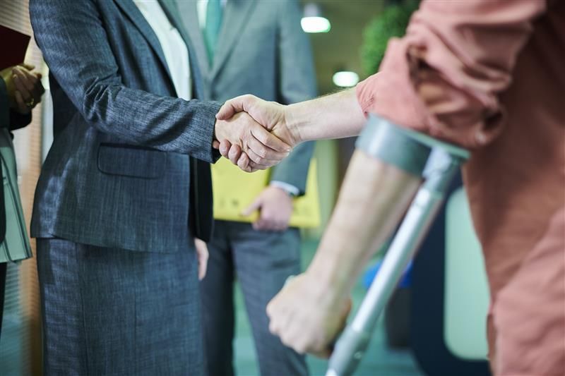 Woman in suit shakes hands with person using crutch.