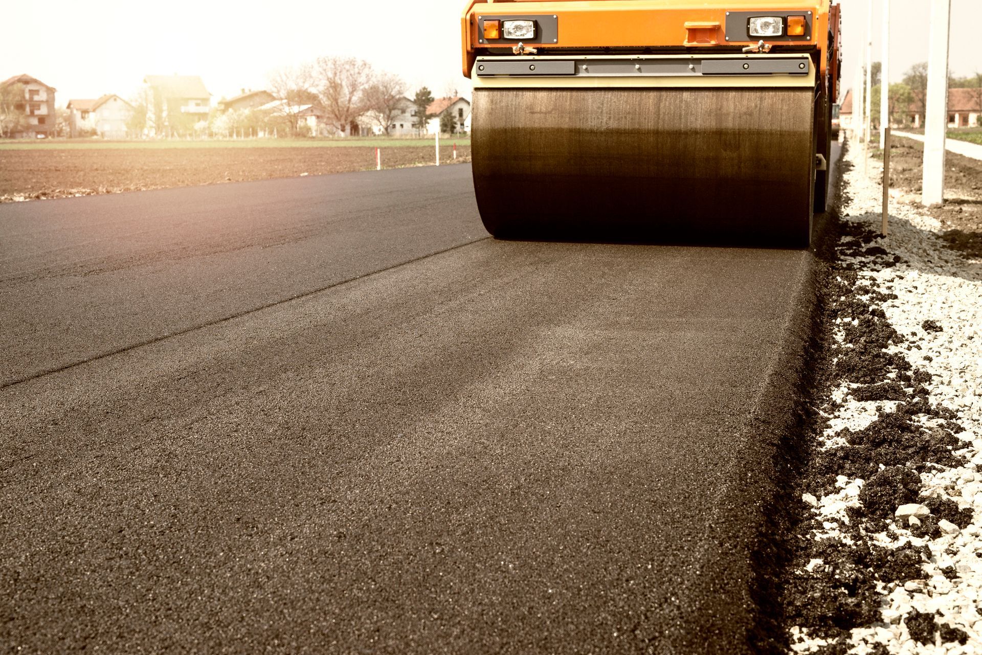 Road roller compacting fresh asphalt on a road. Orange roller, black asphalt. Sunny day.