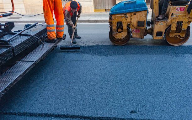 Workers paving a road with asphalt; a roller compacts the fresh surface.
