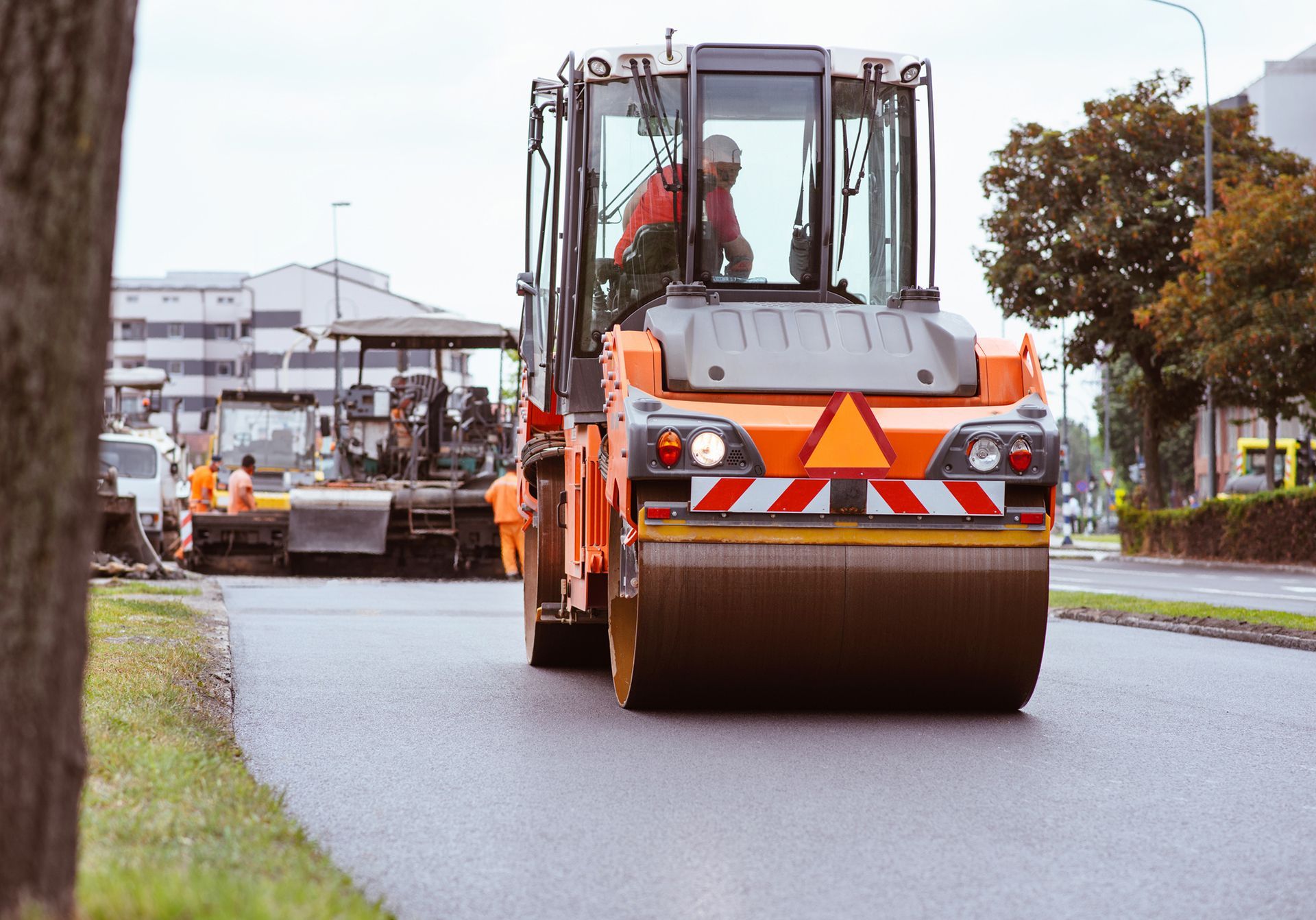 Orange road roller compacting fresh asphalt on a city street. Orange road roller compacting fresh asphalt on a city street.