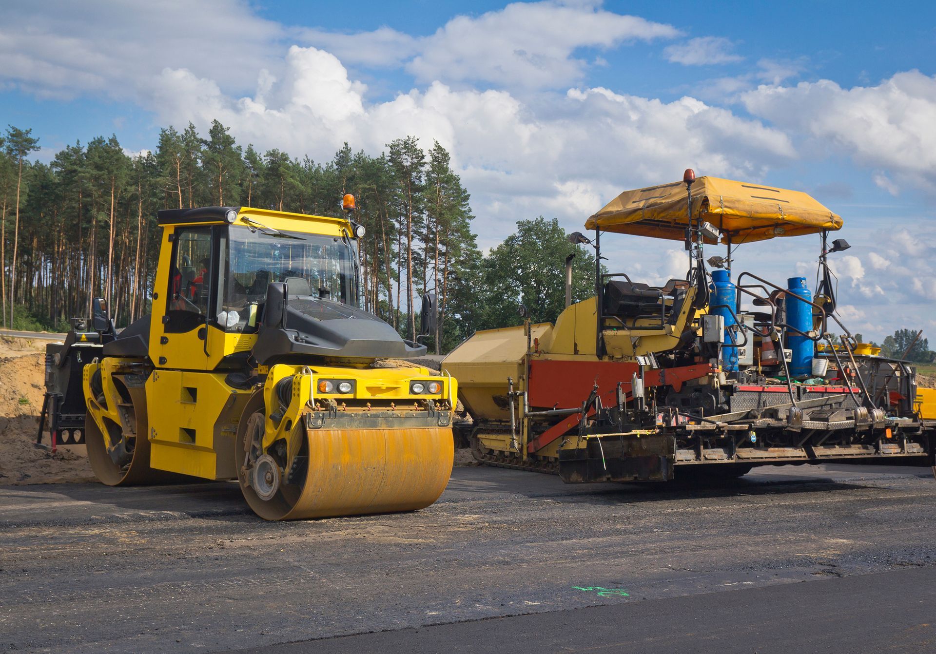 Yellow road roller and paving machine on new asphalt, outdoors.