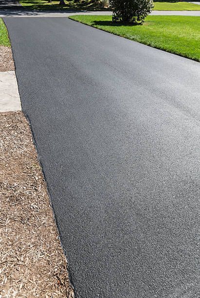 Freshly paved asphalt driveway, dark gray, with green grass on the right and mulch on the left.