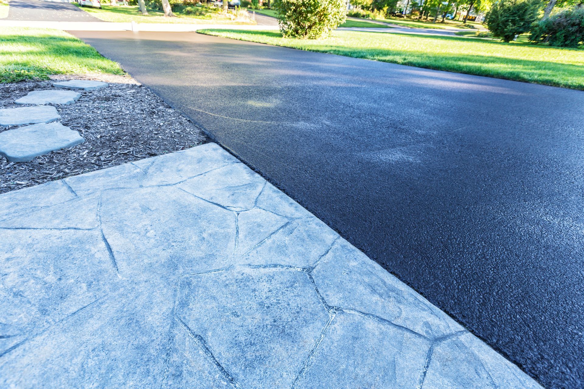 Asphalt driveway next to patterned concrete walkway and grassy lawn.