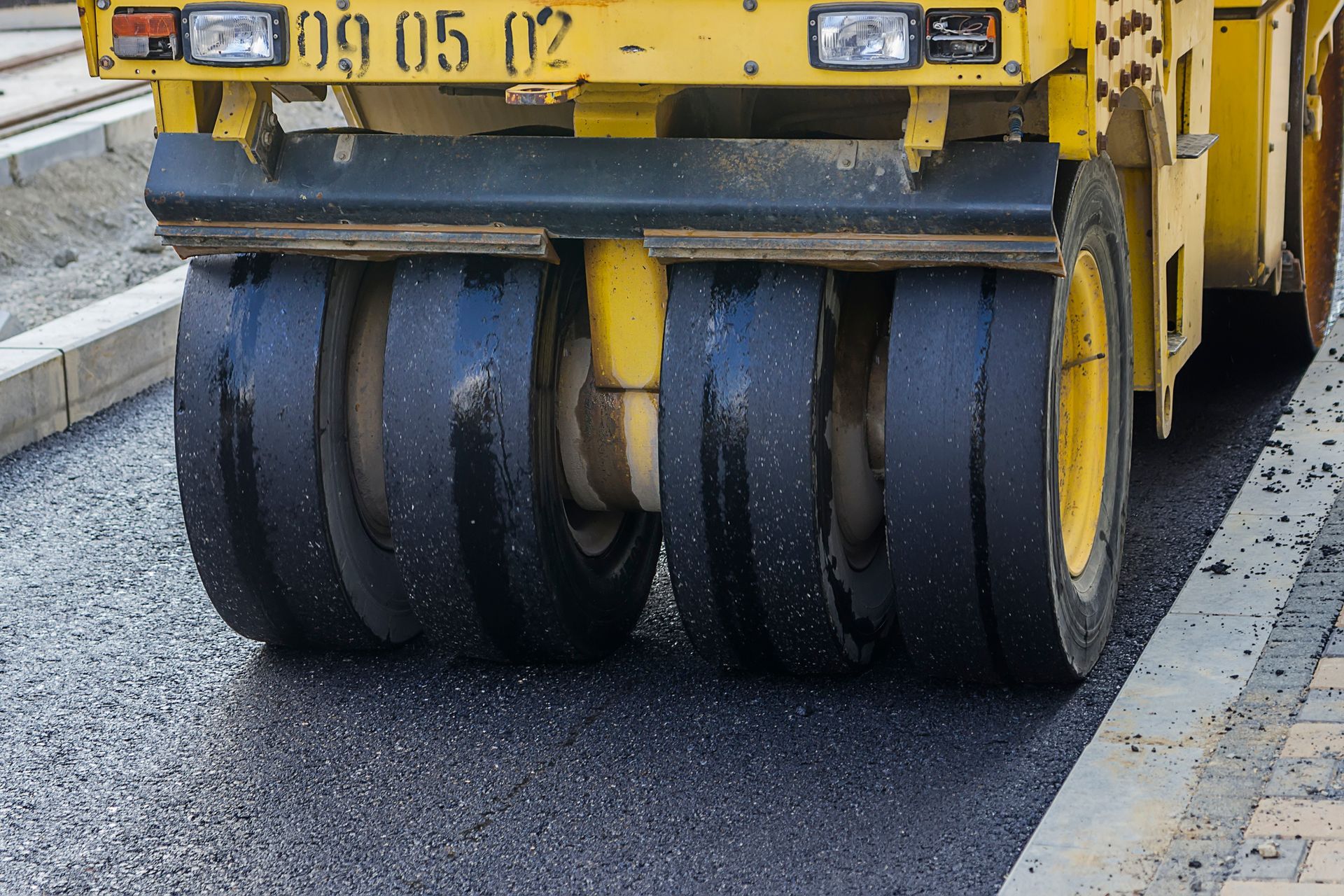 Yellow road roller compacting fresh asphalt on a city street.