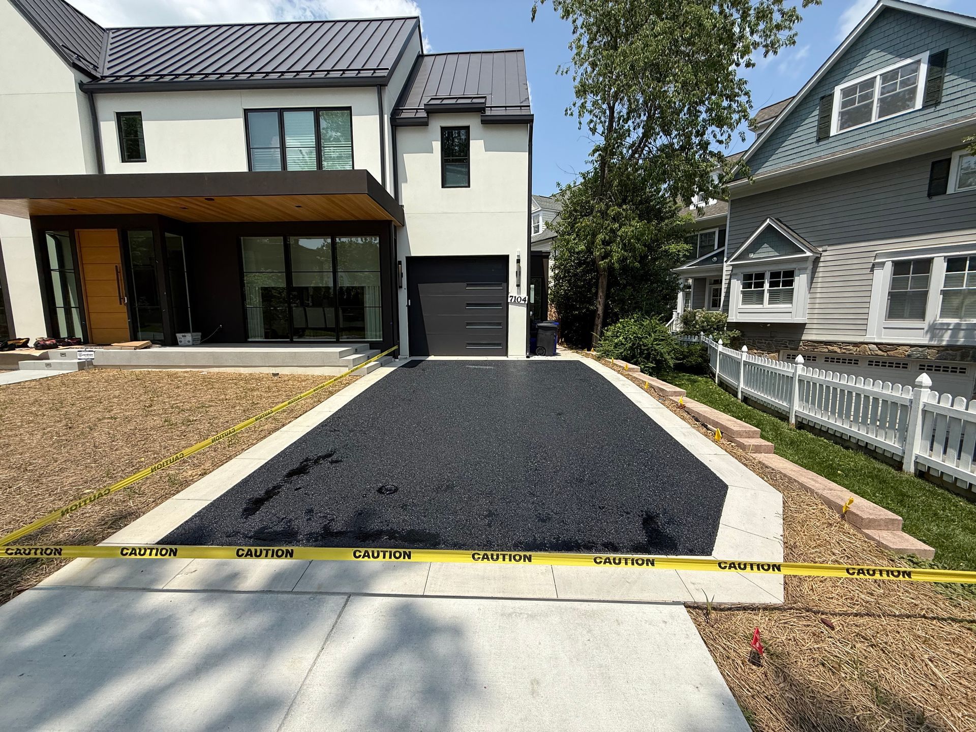 Driveway with black surfacing, between light concrete borders, leading to a garage door. Caution tape in foreground.