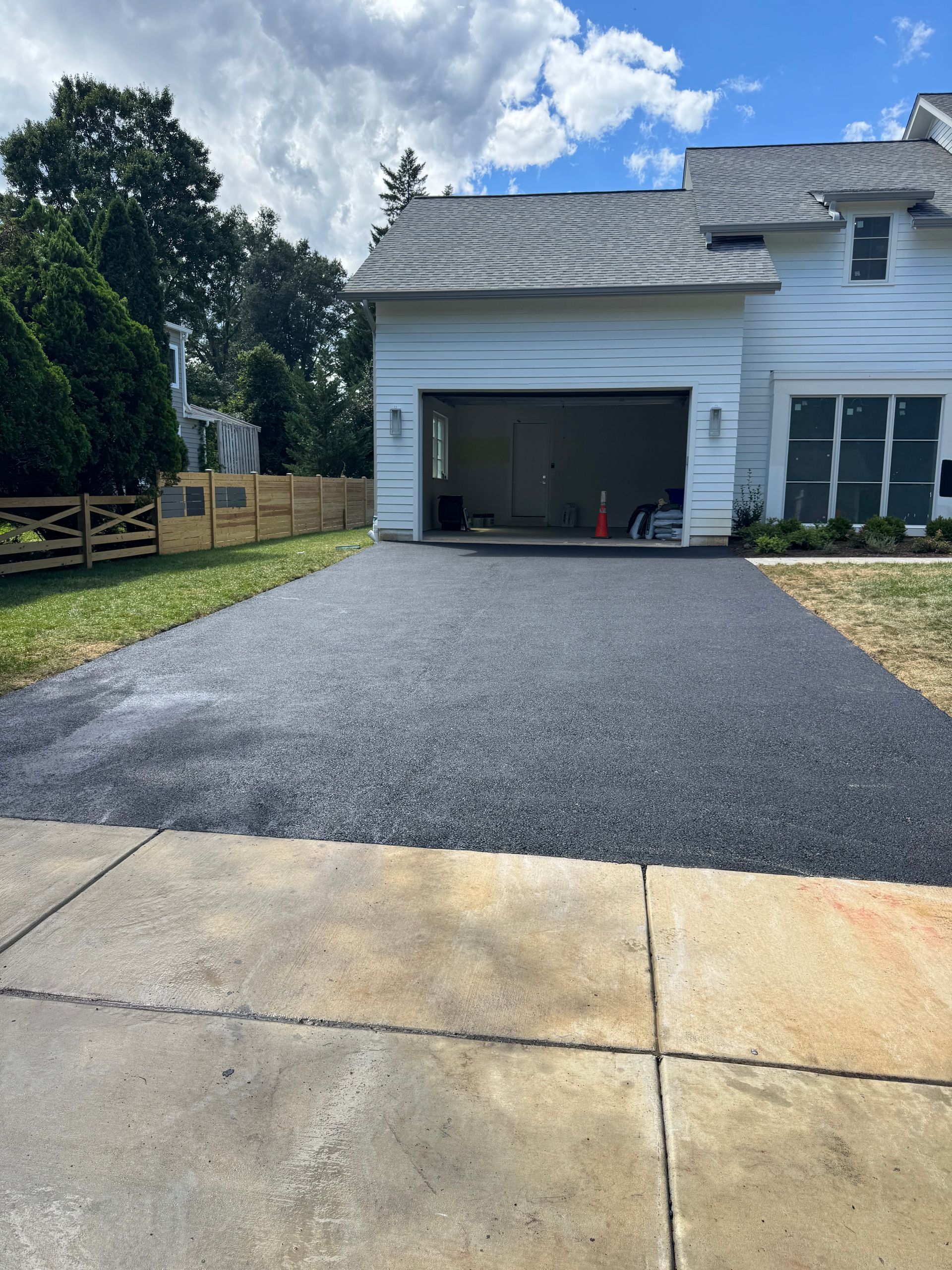 Freshly paved asphalt driveway leading to a white house with an open garage.