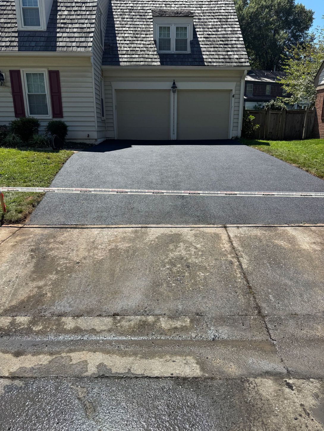 Asphalt driveway freshly sealed, transitioning to a concrete approach in front of a house with a two-car garage.