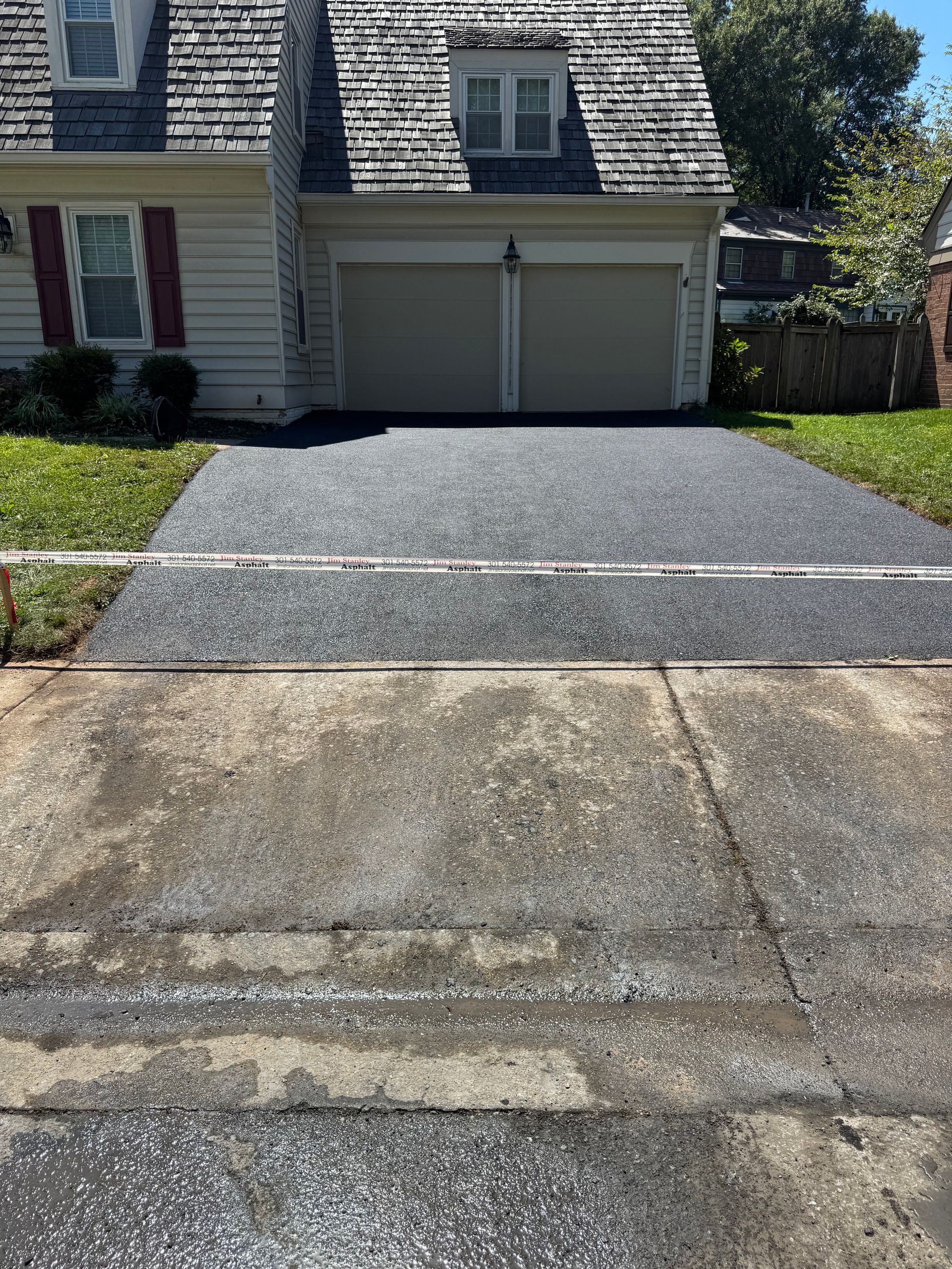 Asphalt driveway freshly sealed, transitioning to a concrete approach in front of a house with a two-car garage.