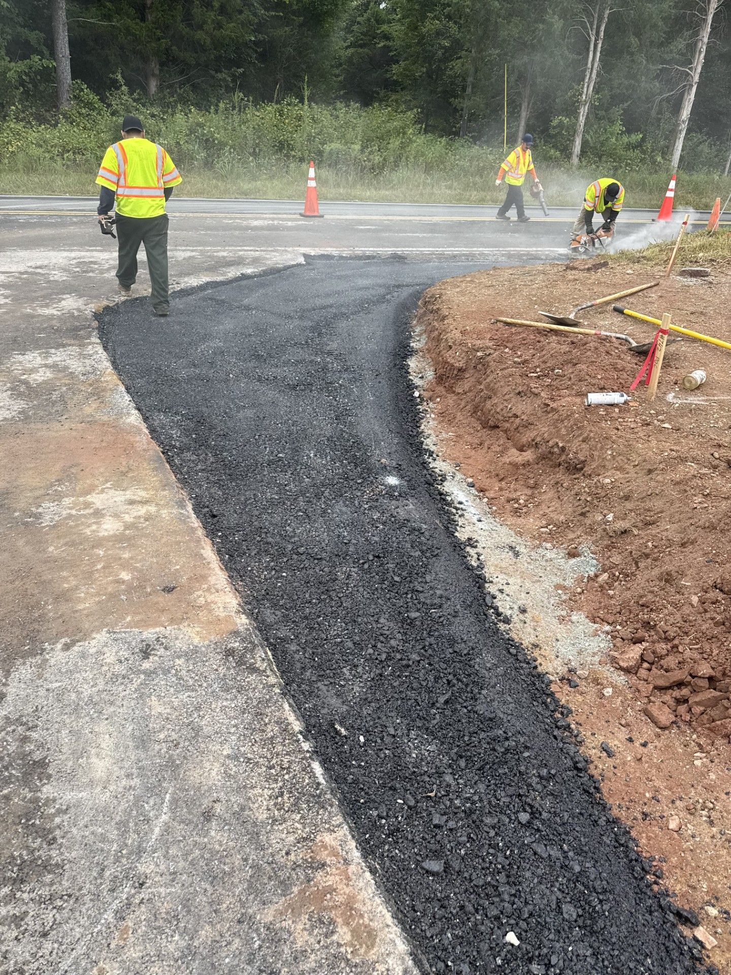 Road workers paving a new asphalt pathway with tools and safety vests.