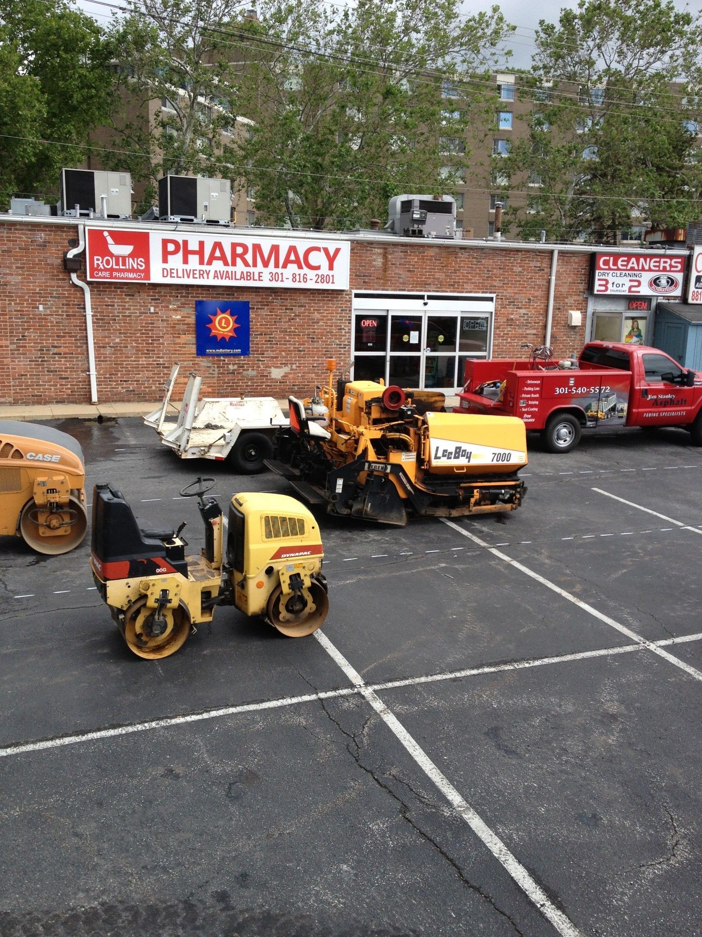Construction equipment parked in front of a brick building with a pharmacy sign.