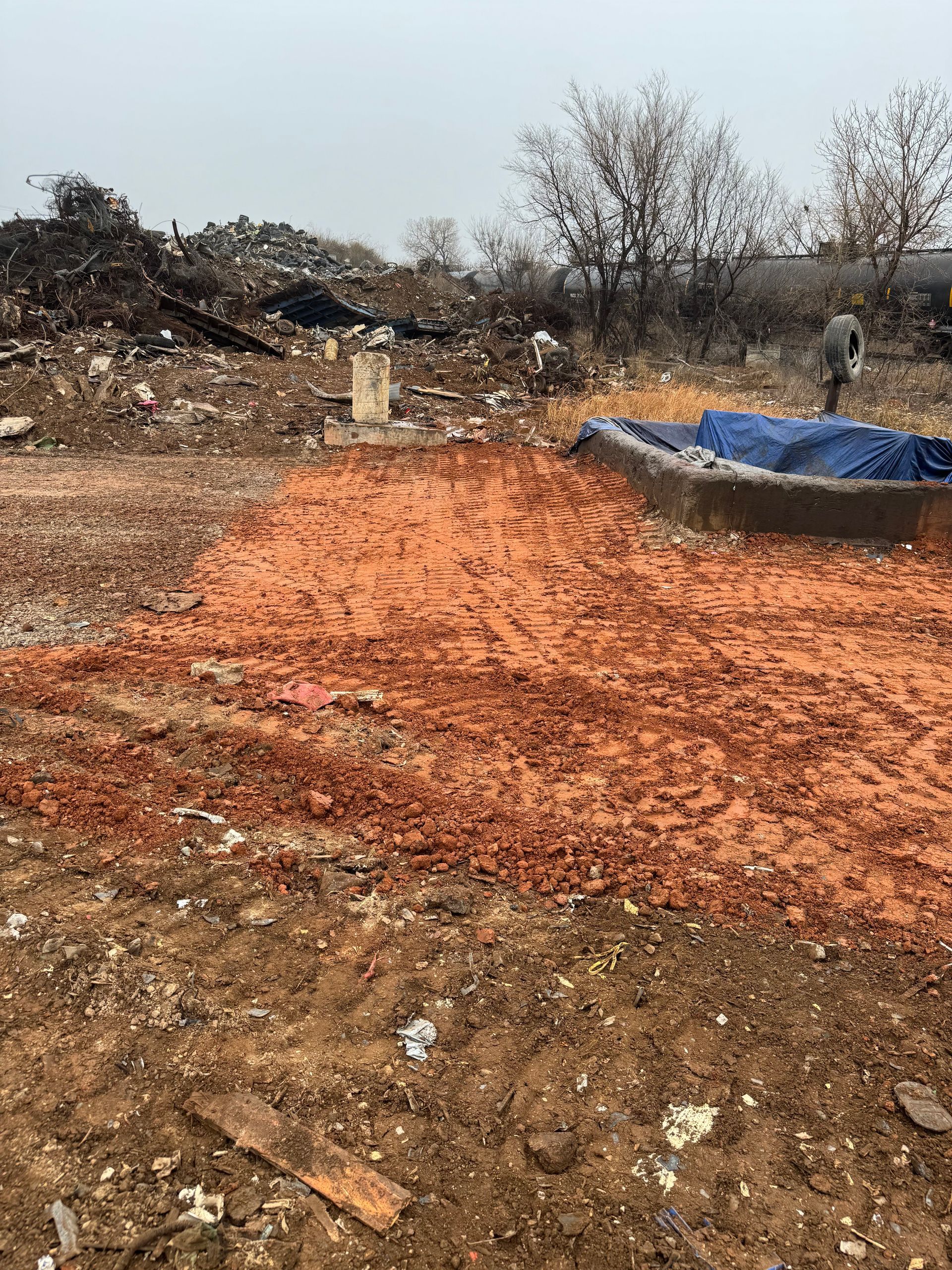 Skid steer with grapple arm lifting a tree trunk near a house with a wooden deck and bare trees.