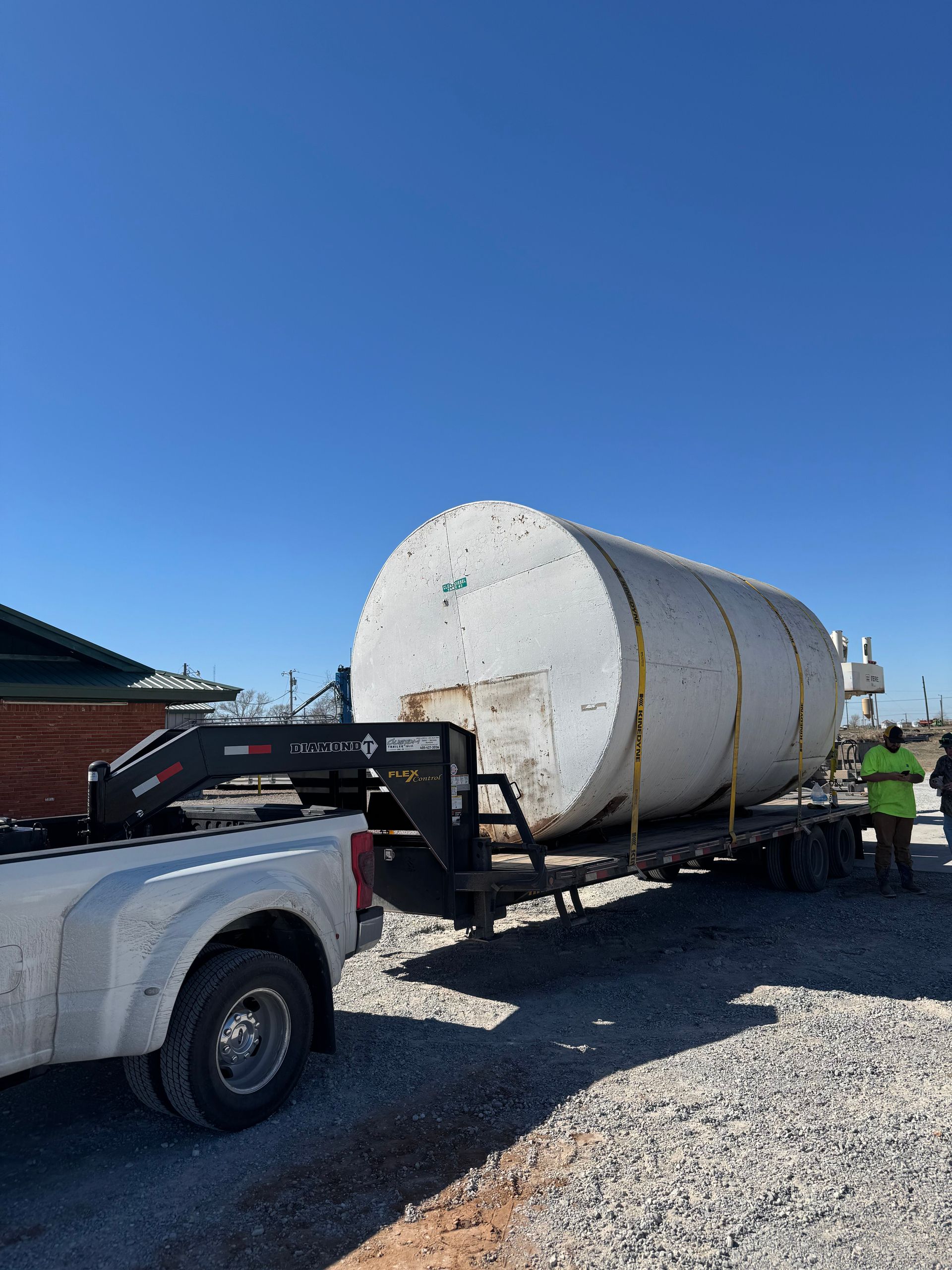 Skid steer with grapple arm lifting a tree trunk near a house with a wooden deck and bare trees.
