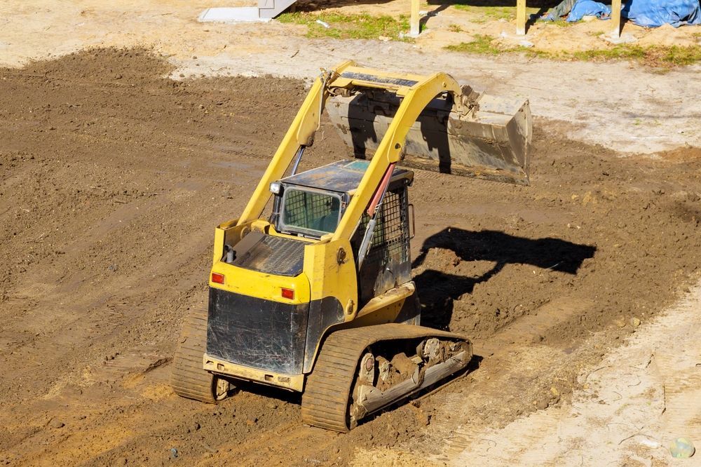 Yellow skid steer operating on a construction site, moving dirt.