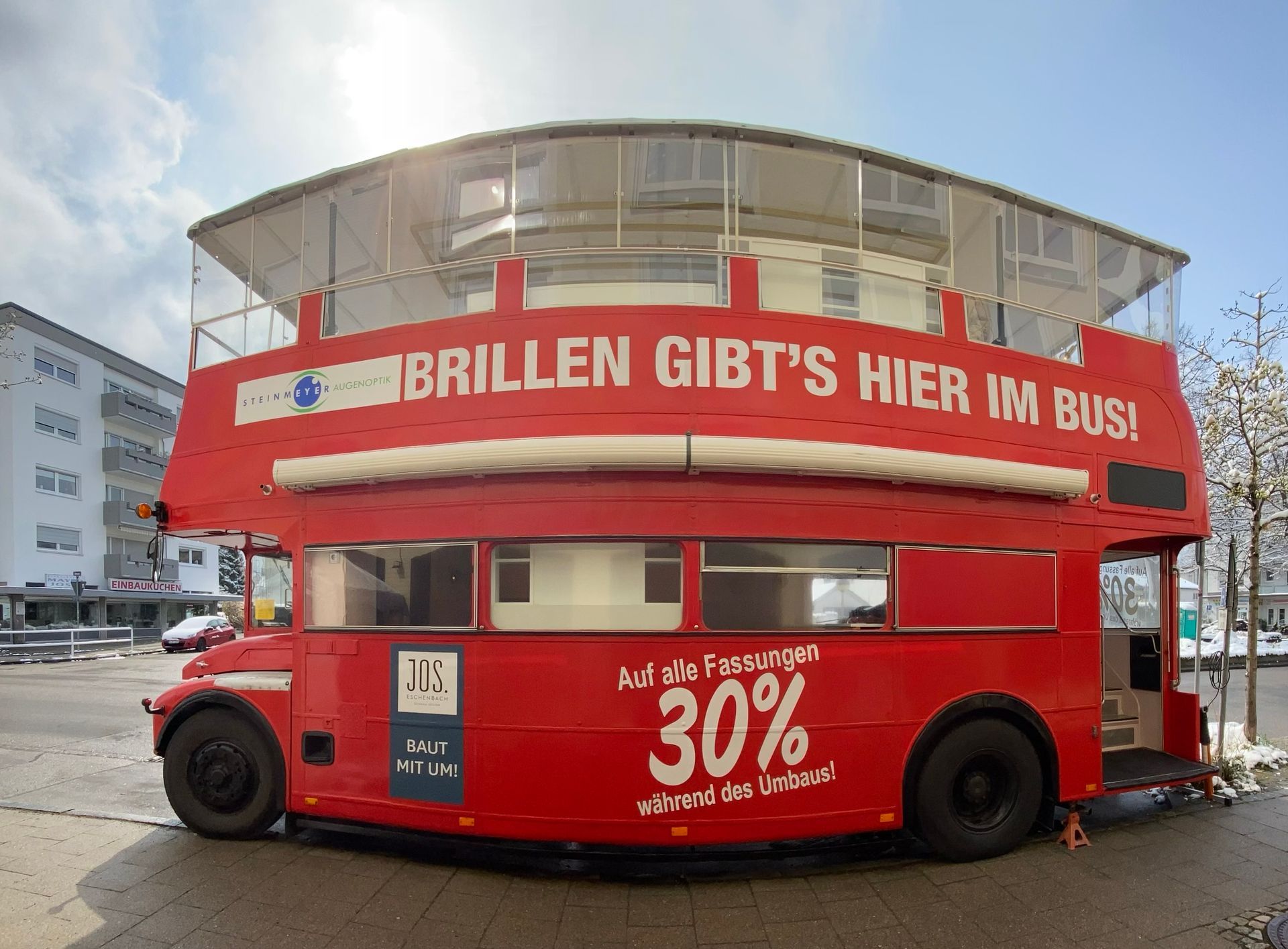 A red double decker bus that says brillen gibt 's hier im bus