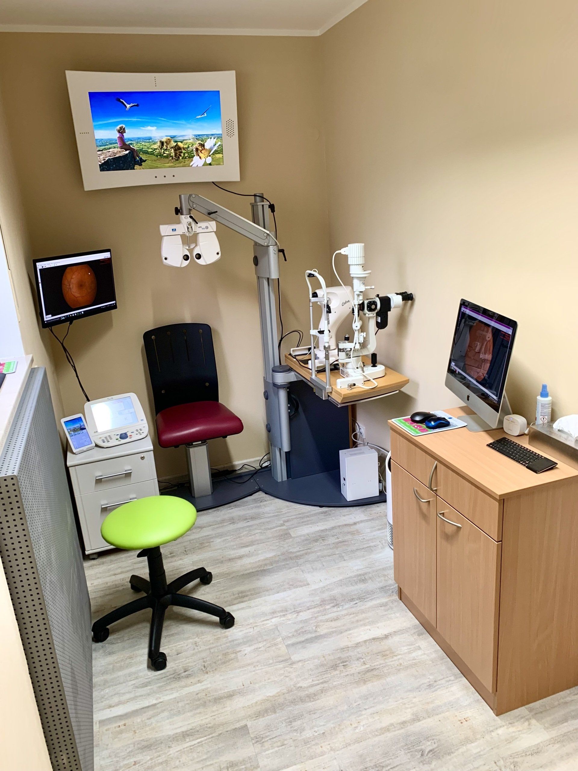 Eine Augenarztpraxis mit einem Computer und einem Monitor an der Wand.