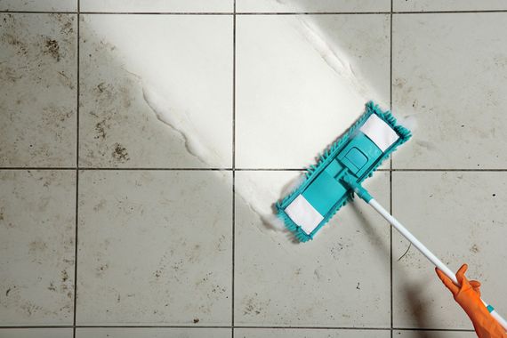 Person mopping a tiled floor with a teal mop head and orange handle Person mopping a tiled floor with a teal mop head and orange handle