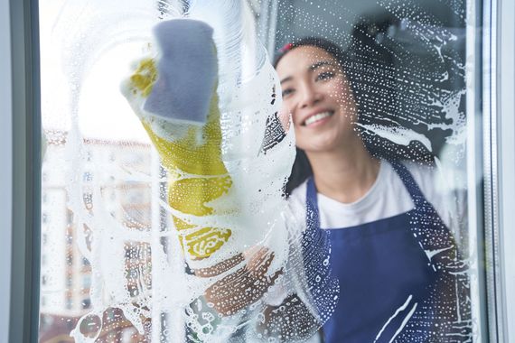 Woman in blue apron cleaning a window with a sponge, smiling amid soap suds. Woman in blue apron cleaning a window with a sponge, smiling amid soap suds.
