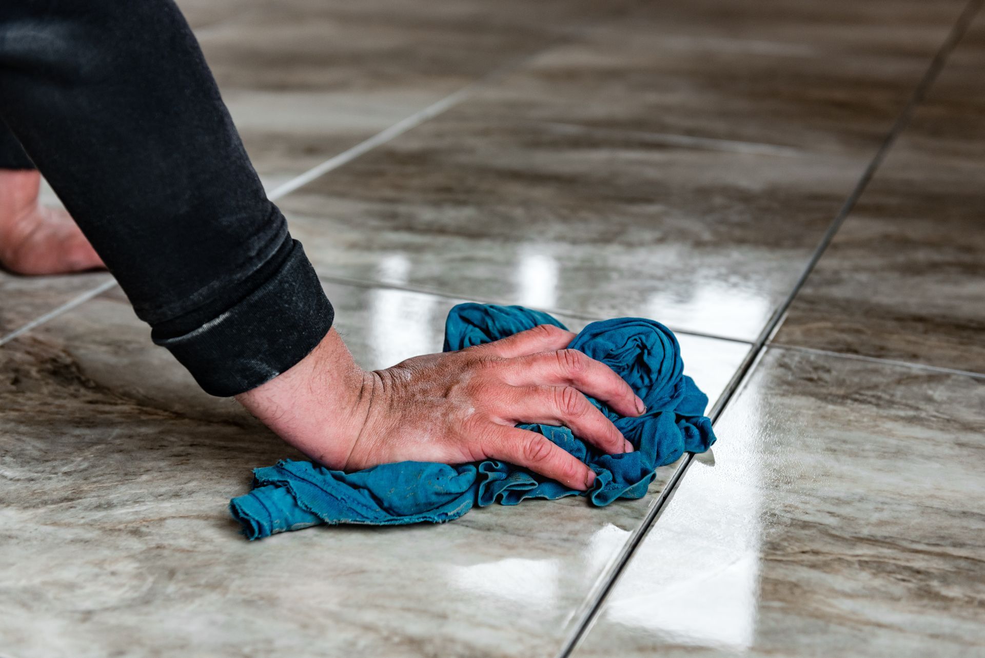 Hand wiping a tiled floor with a blue cloth