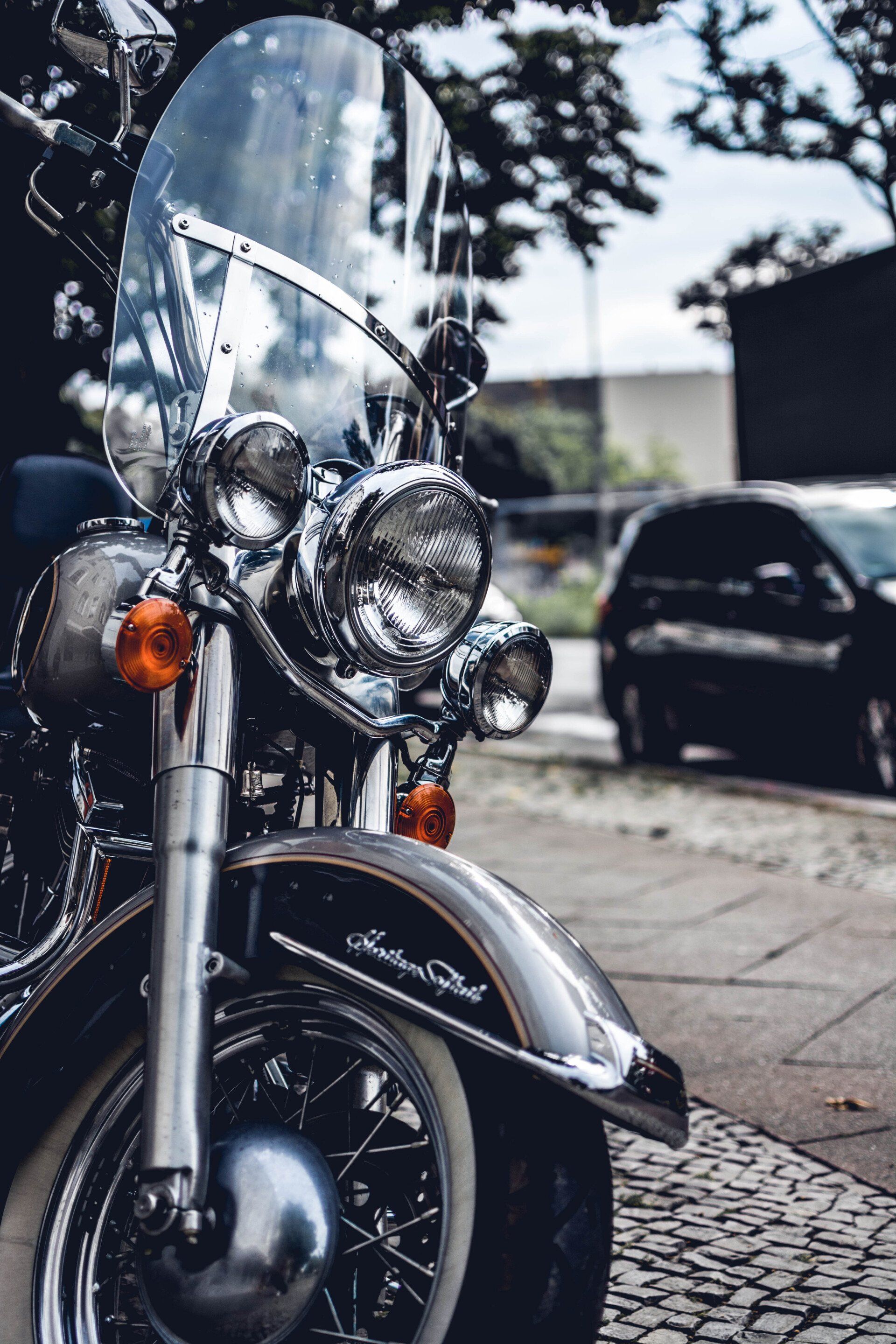 A motorcycle with a windshield is parked on a sidewalk next to a car.