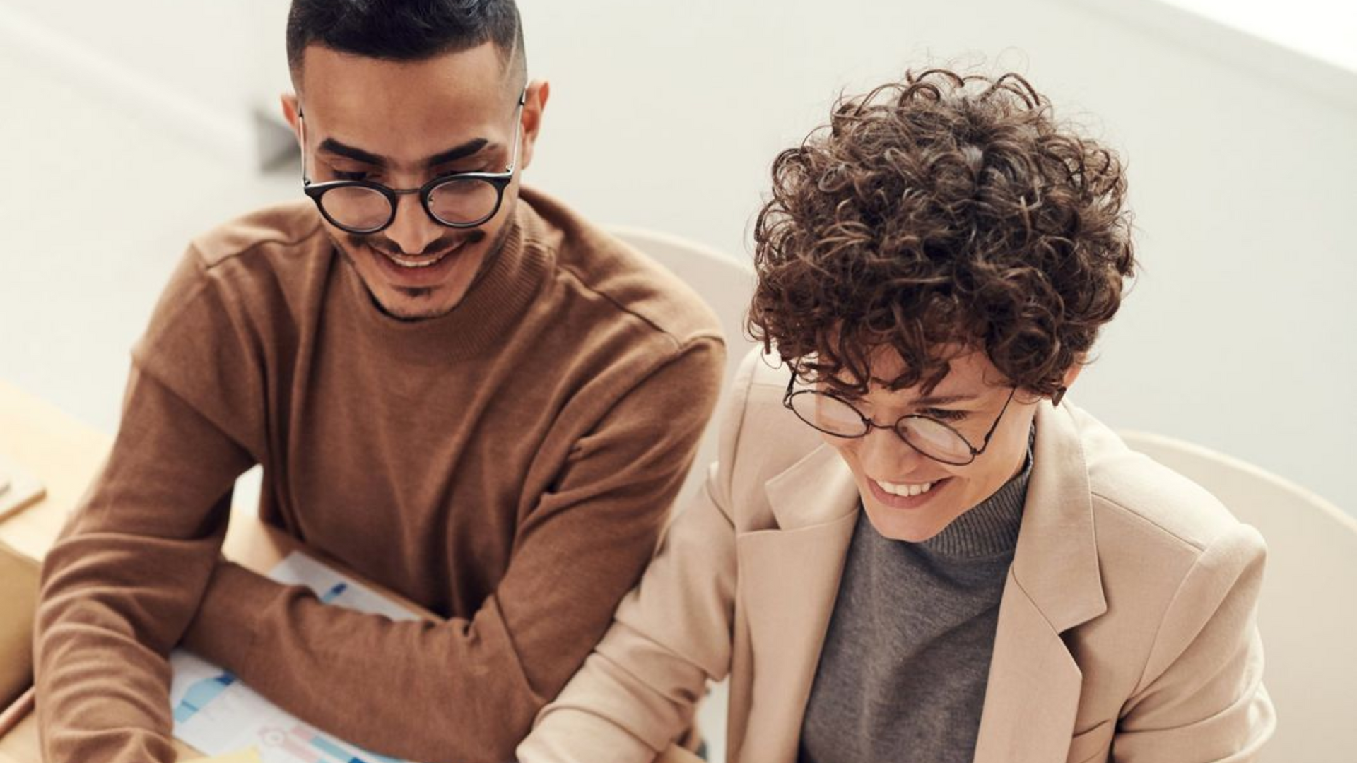 Two people smiling and looking down at a document in a bright office setting