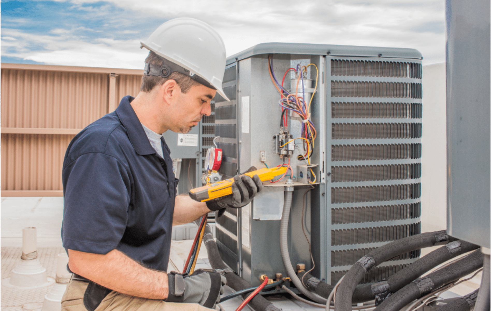 Technician in hard hat using a drill to repair an outdoor HVAC unit with exposed wiring
