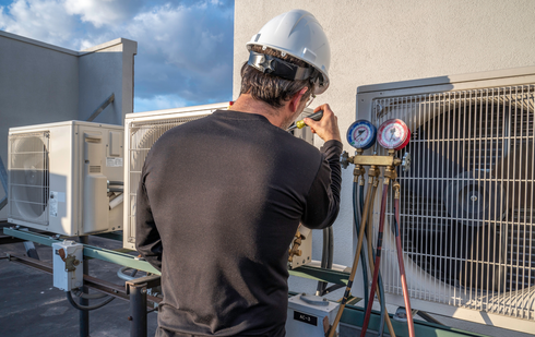 Technician in a hard hat inspecting rooftop HVAC units with gauges and tools