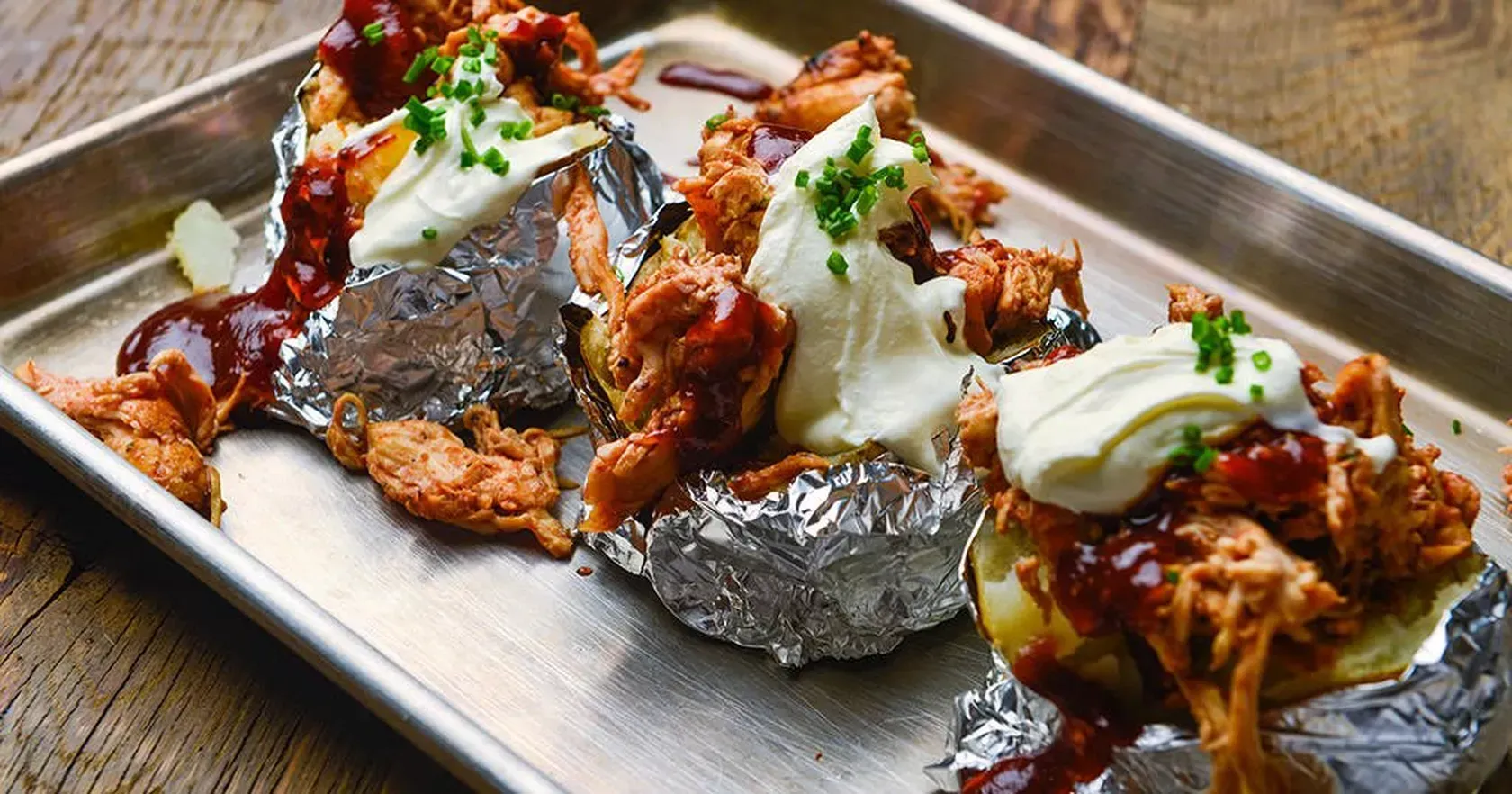 A tray of baked potatoes with meat and sauce on a wooden table.
