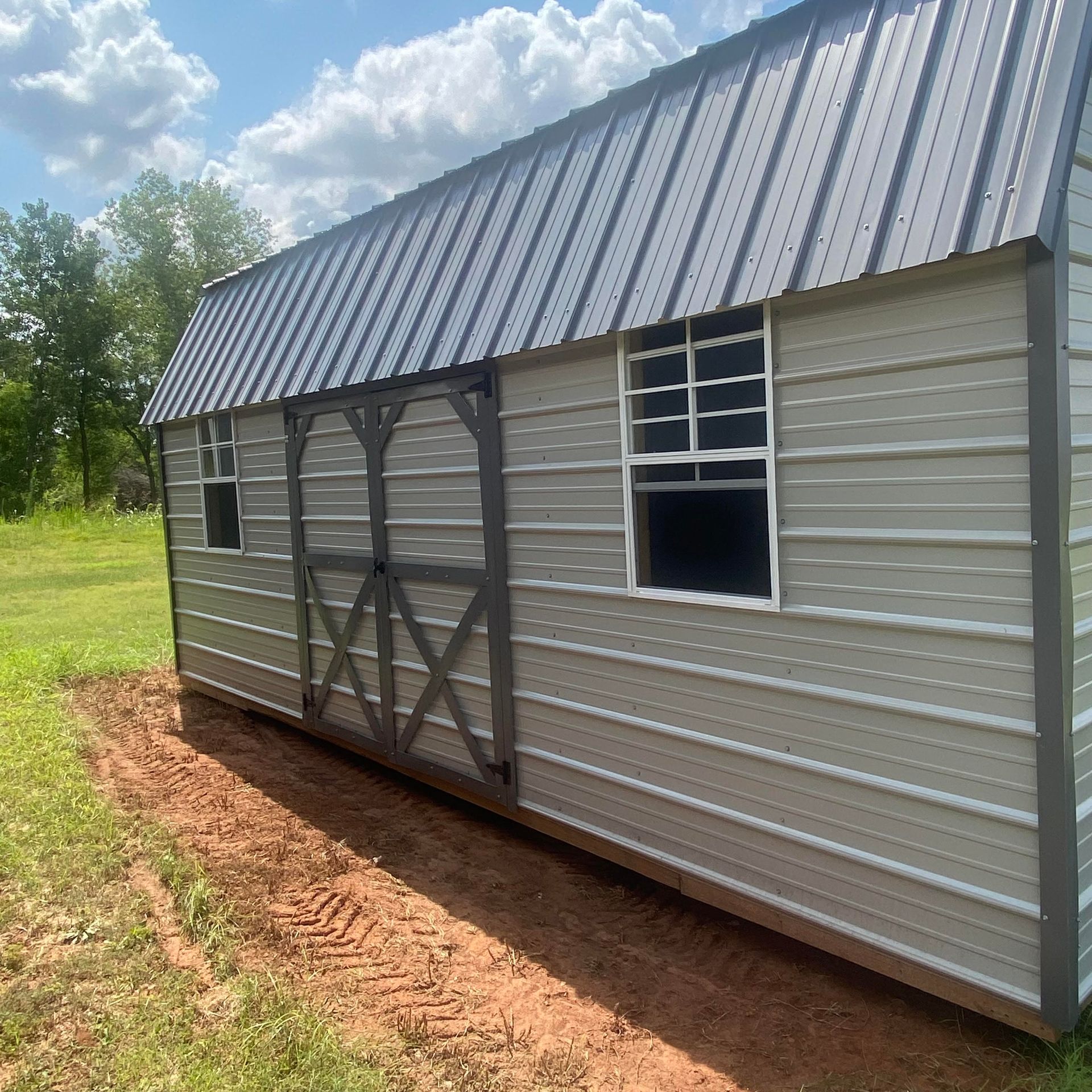 A shed with an ash gray siding a charcoal roof and charcoal trim with a double barn door is sitting in the middle of a field.