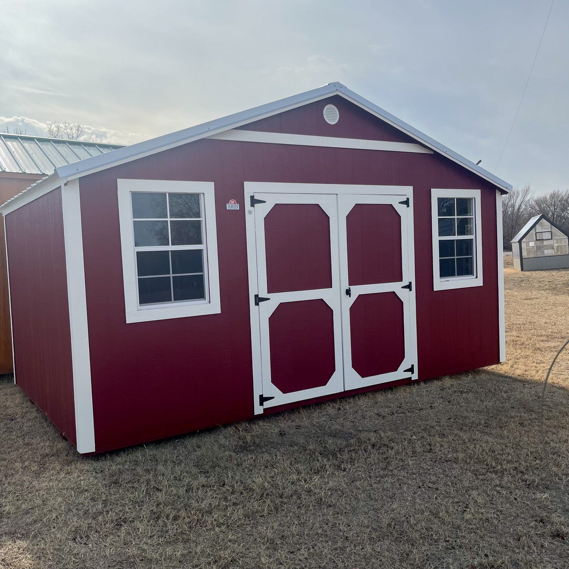 En un campo hay un cobertizo rojo con adornos blancos y ventanas.