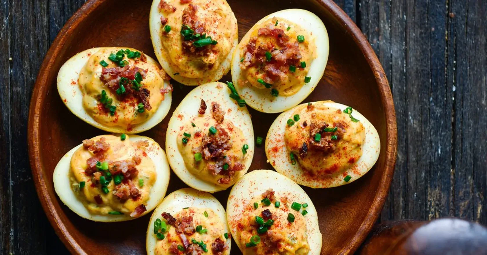 A wooden plate topped with stuffed eggs on a wooden table.