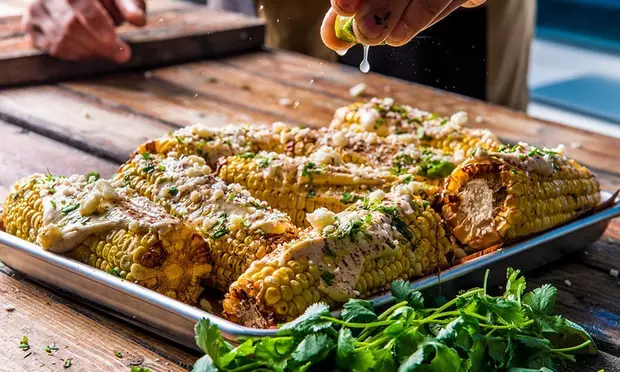 A person is squeezing lime juice on corn on the cob.