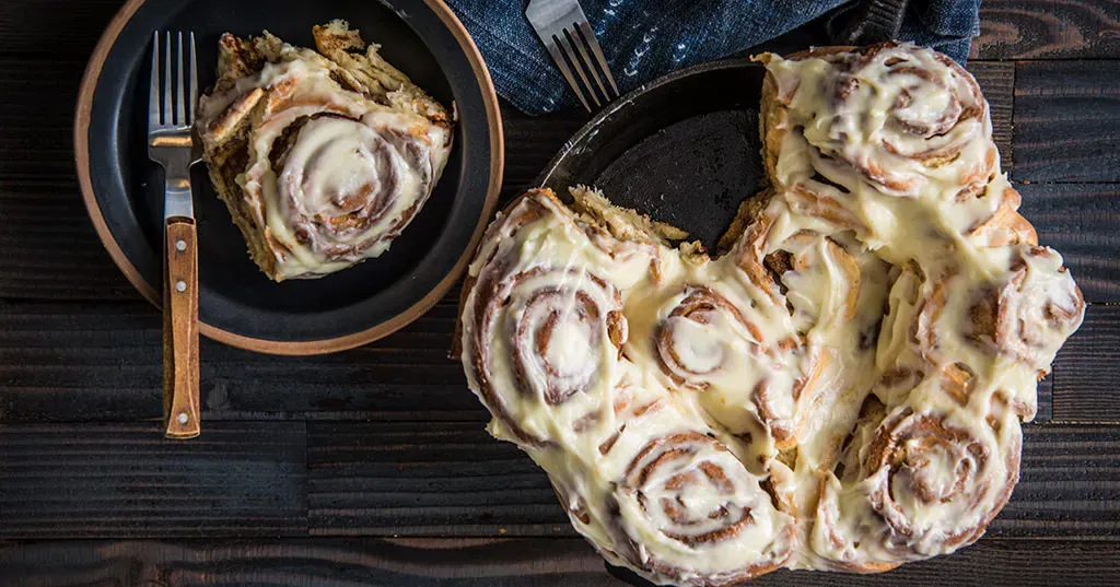 A bunch of cinnamon rolls on a plate with a fork on a wooden table.