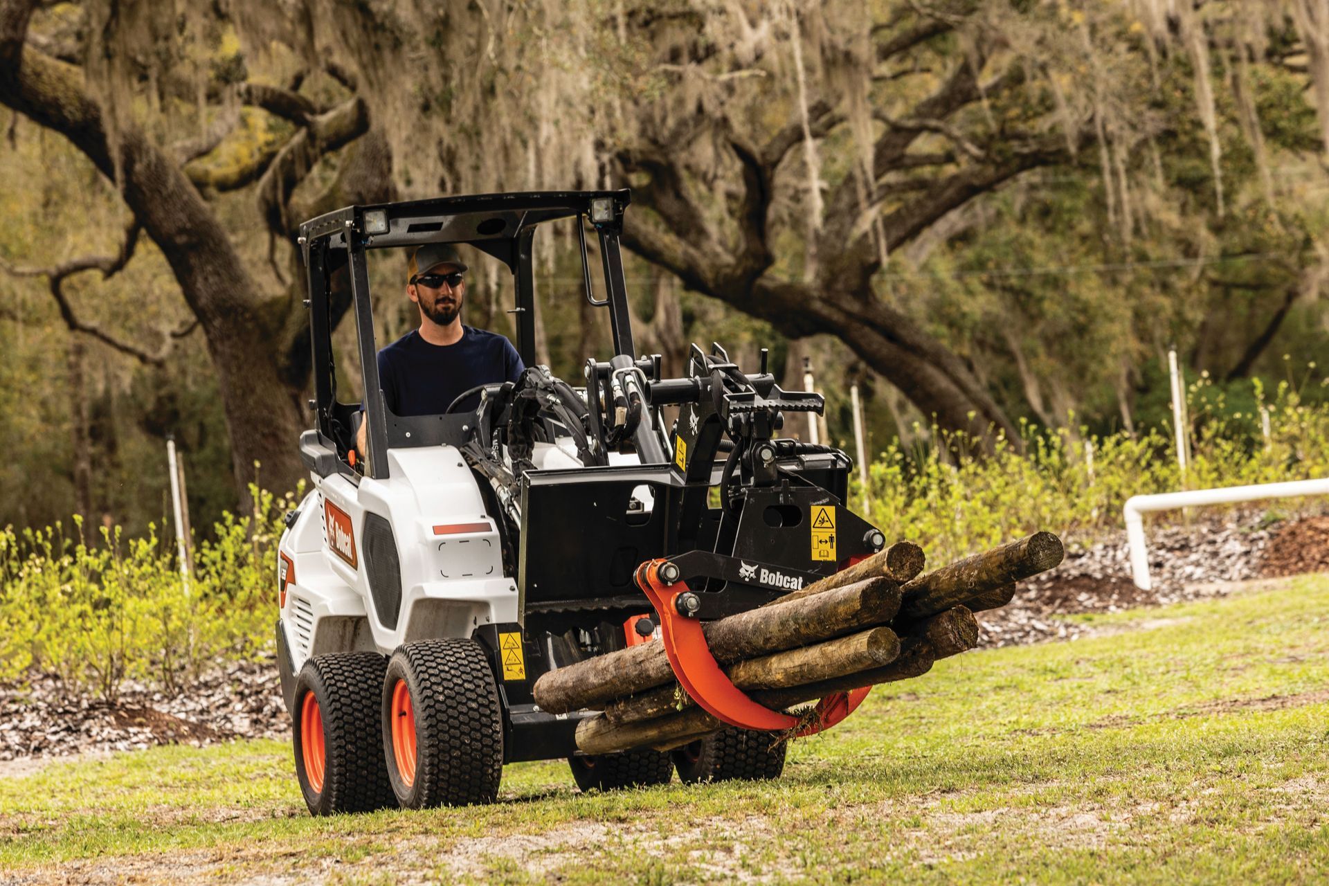a man is driving a bobcat tractor carrying logs