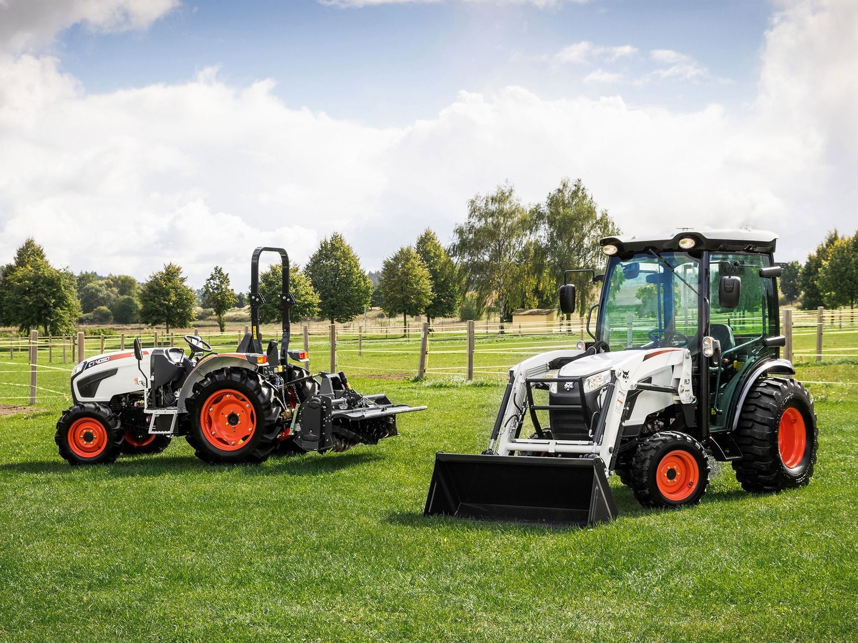 two bobcat tractors are parked in a grassy field