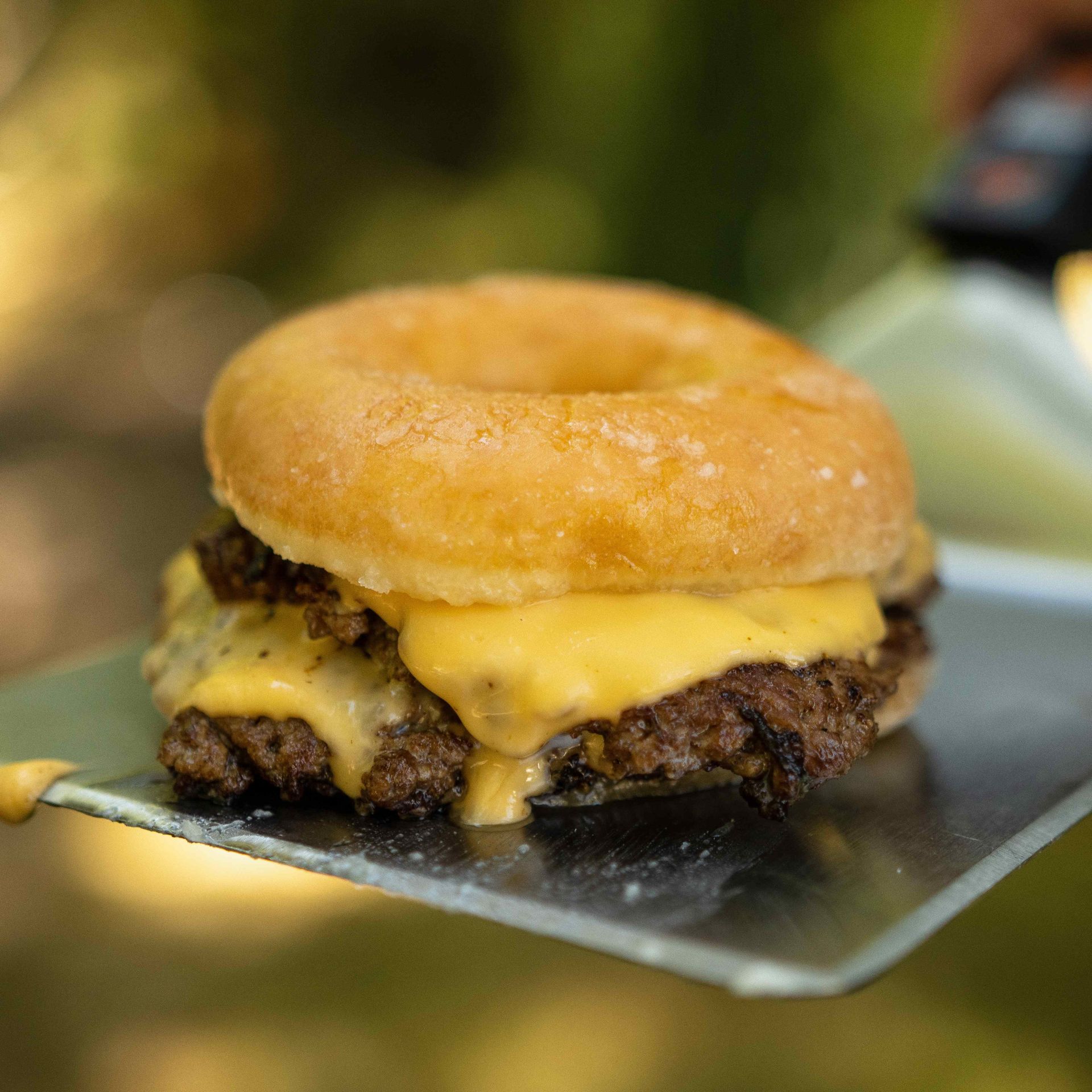 A person is holding a donut shaped hamburger on a spatula.