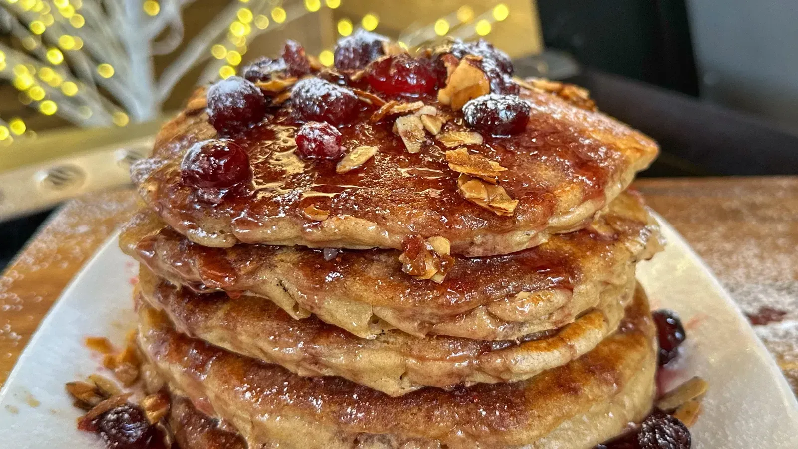 A stack of pancakes with cranberries and powdered sugar on a white plate.