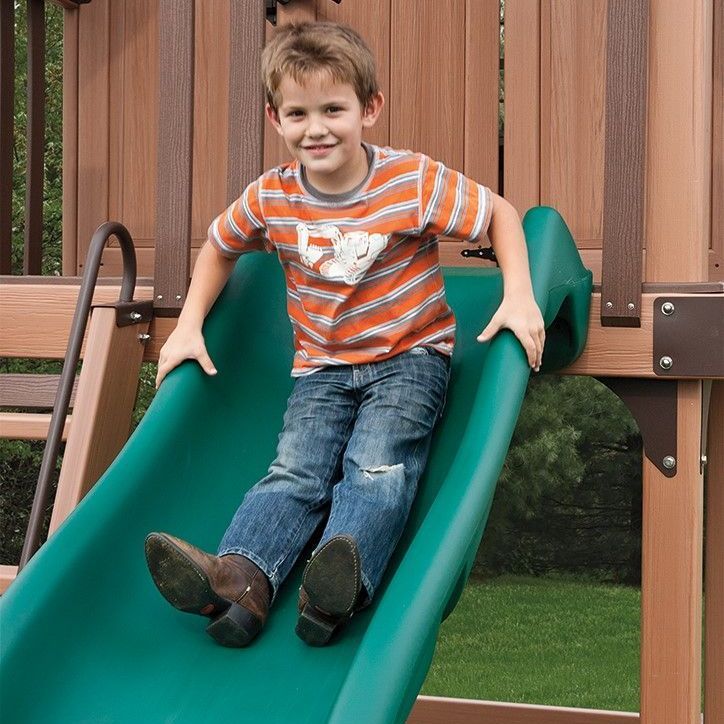 a young boy is sitting on a green slide wearing cowboy boots