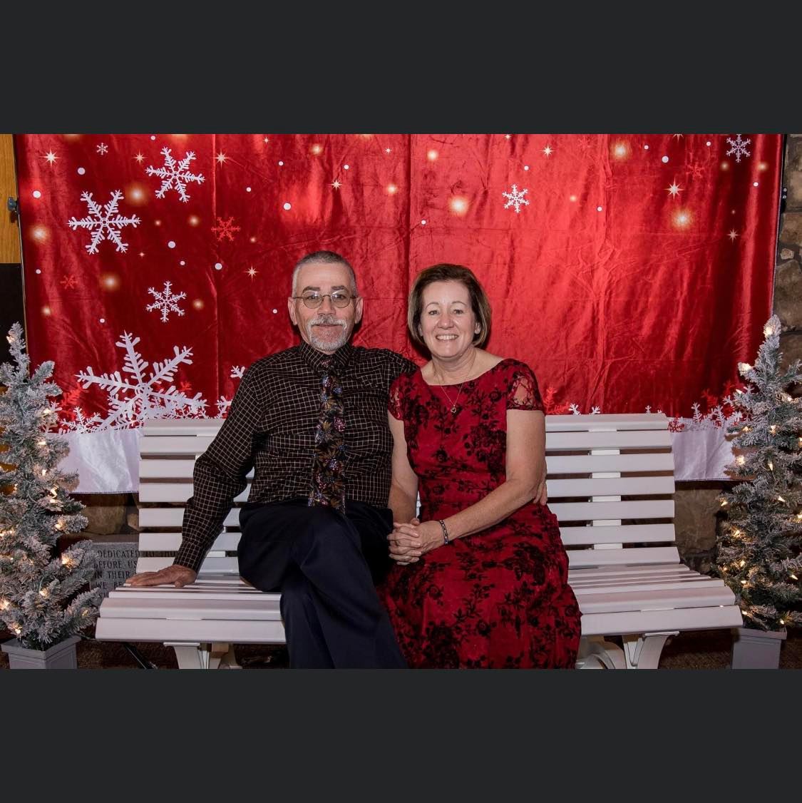 A man and a woman are sitting on a bench in front of a christmas backdrop.