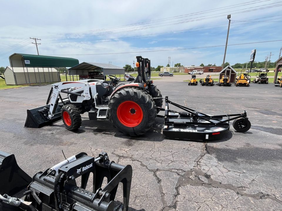 A tractor with a mower attached to it is parked in a parking lot.