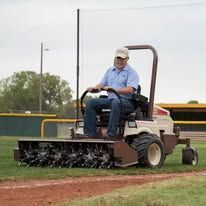 A man is riding a lawn mower on a baseball field.