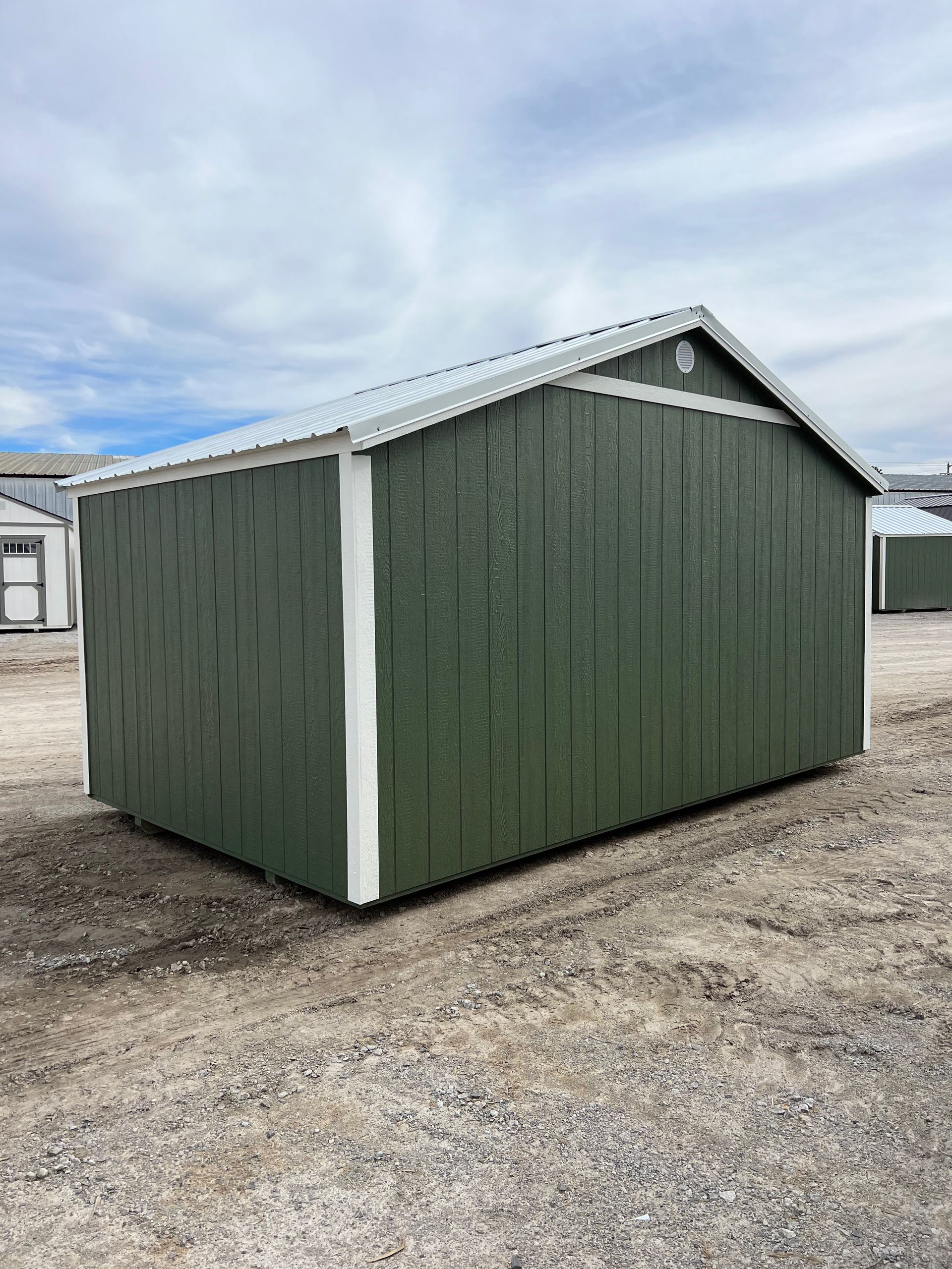 A green shed with a white trim is sitting on top of a dirt field.