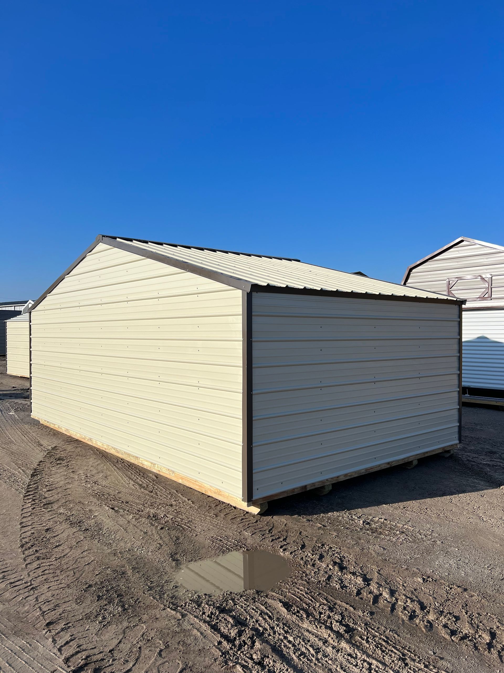 A white metal garage is sitting in the middle of a dirt field.