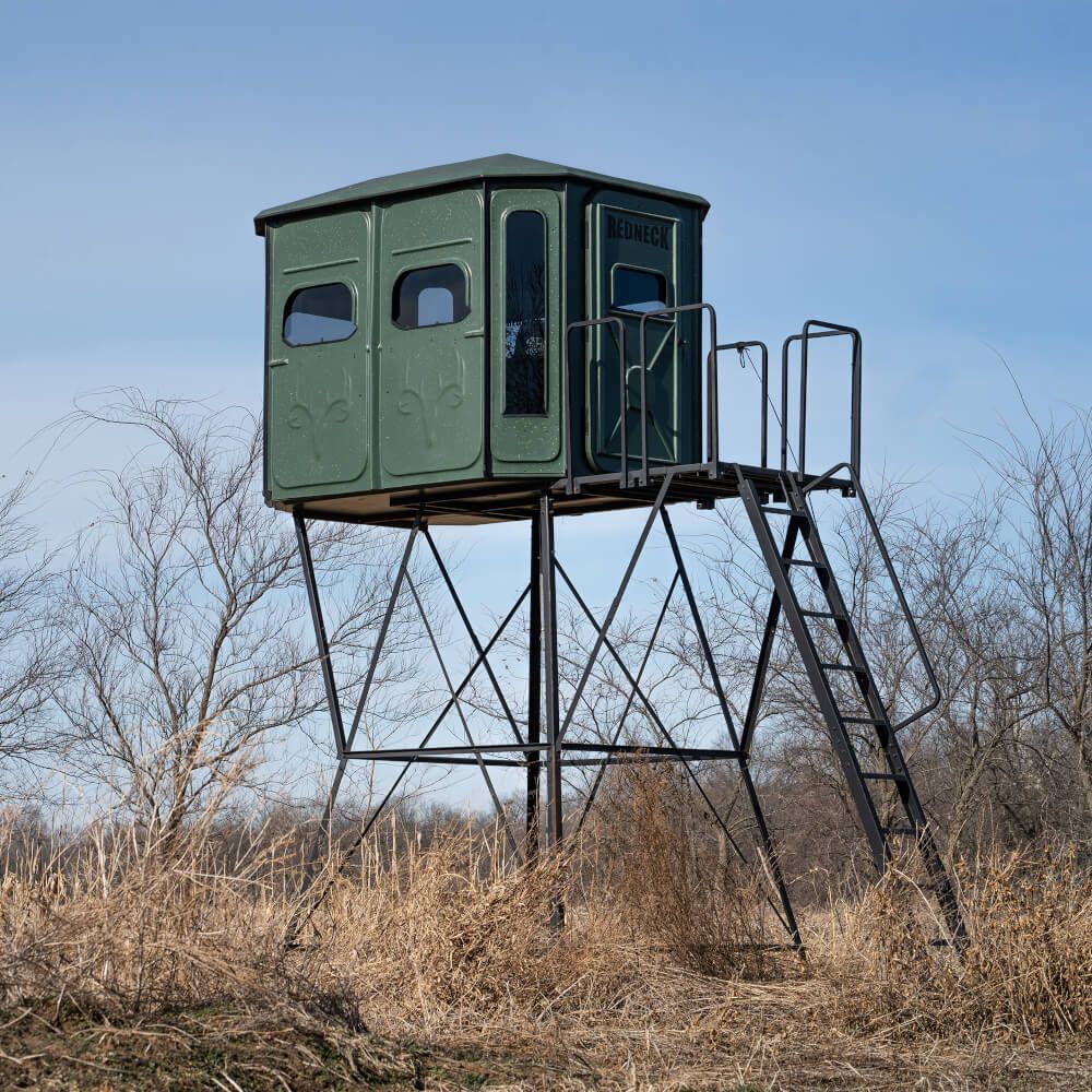 A green hunting blind with a ladder on top of it in a field.