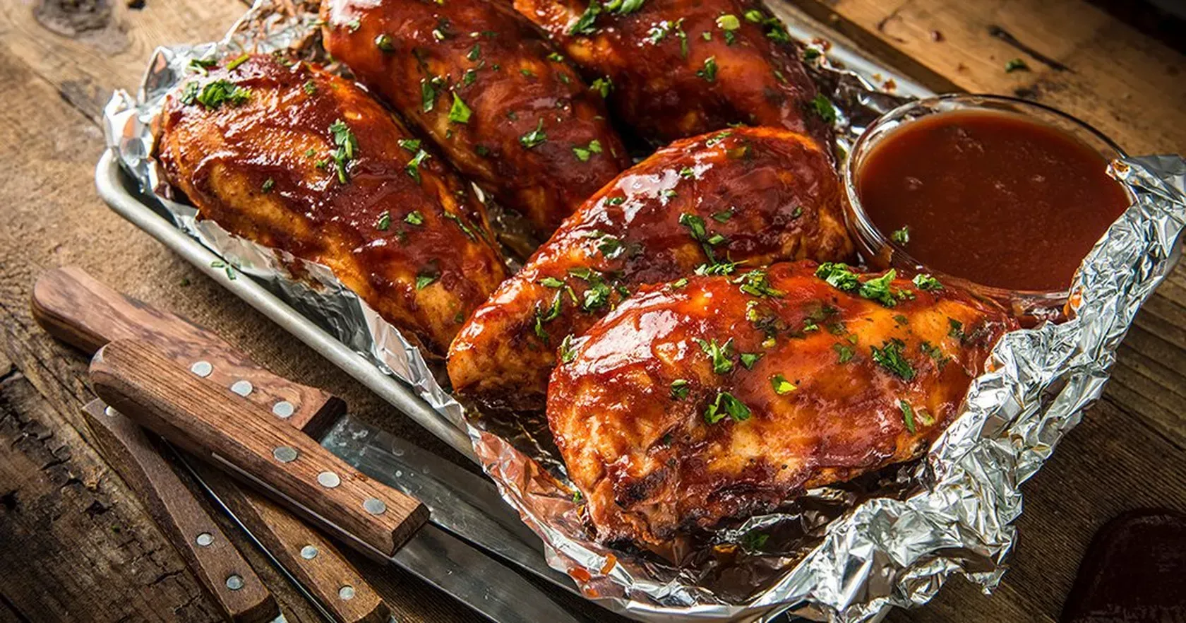 The chicken is wrapped in tin foil and covered in barbecue sauce.