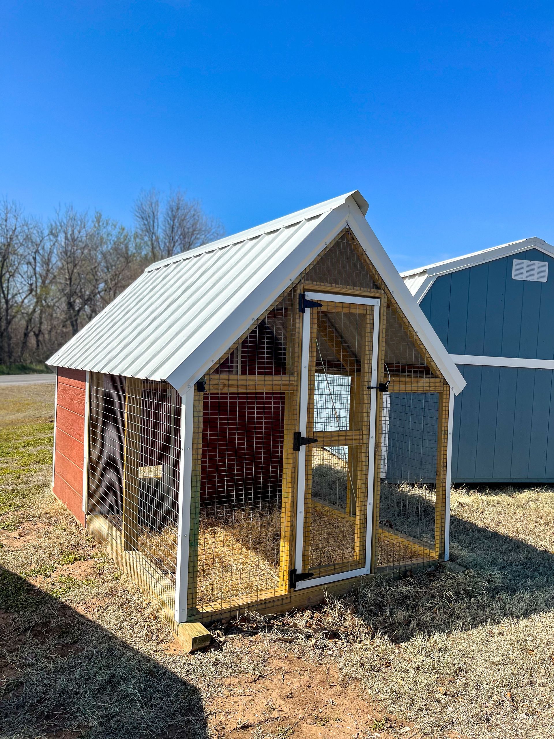 A small wooden chicken coop with a metal roof is sitting on top of a dirt field.