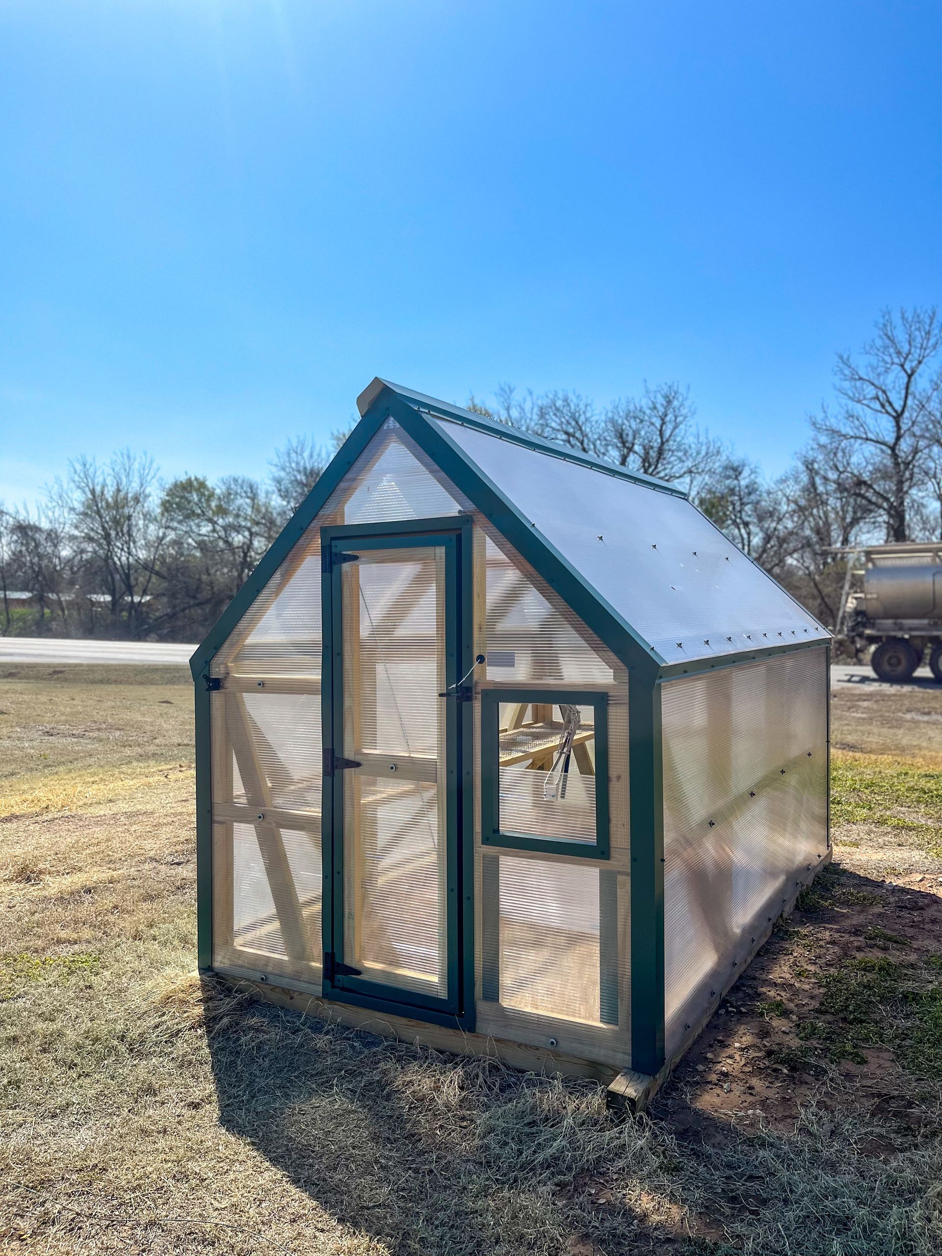 A greenhouse is sitting in the middle of a dirt field.
