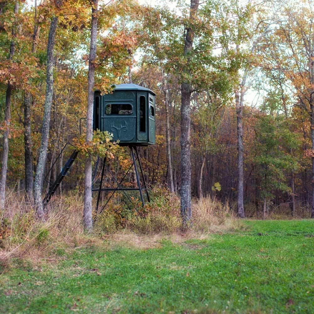 A green deer stand in the middle of a field in the woods.