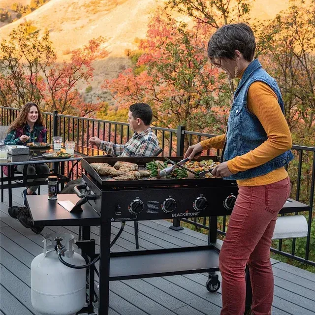 A woman is cooking food on a grill on a deck.