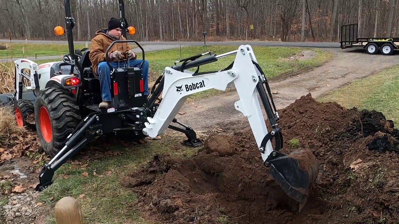 A man is driving a bobcat tractor with a backhoe attached to it.