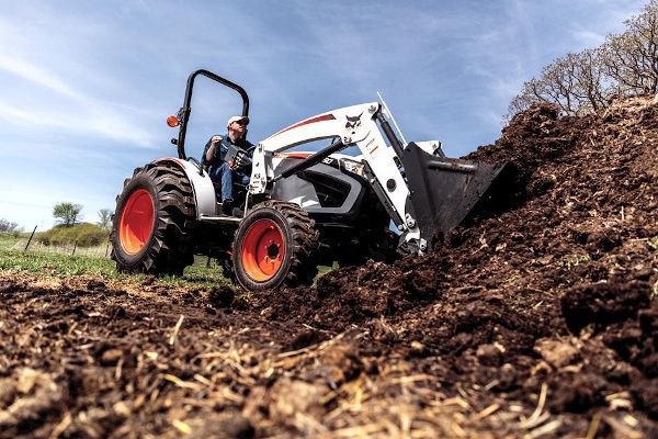 a man is driving a bobcat tractor carrying logs